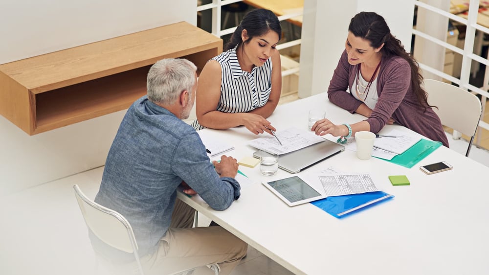 Ein Team von drei Marketingexperten (zwei Frauen und ein Mann) analysiert gemeinsam einen gedruckten Bericht über die Marketingdaten des letzten Zeitraums.