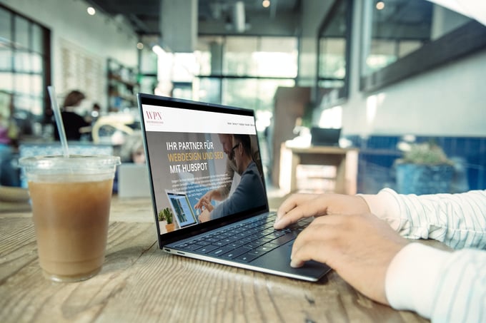 Mann im Büro nutzt seinen Laptop, auf dem Tisch steht ein Glas Kaffee.