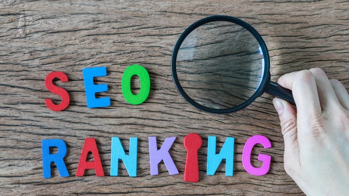 SEO RANKING auf braunem Hintergrund mit Hand und Lupe – Bedeutung von SEO-Rankings hervorheben